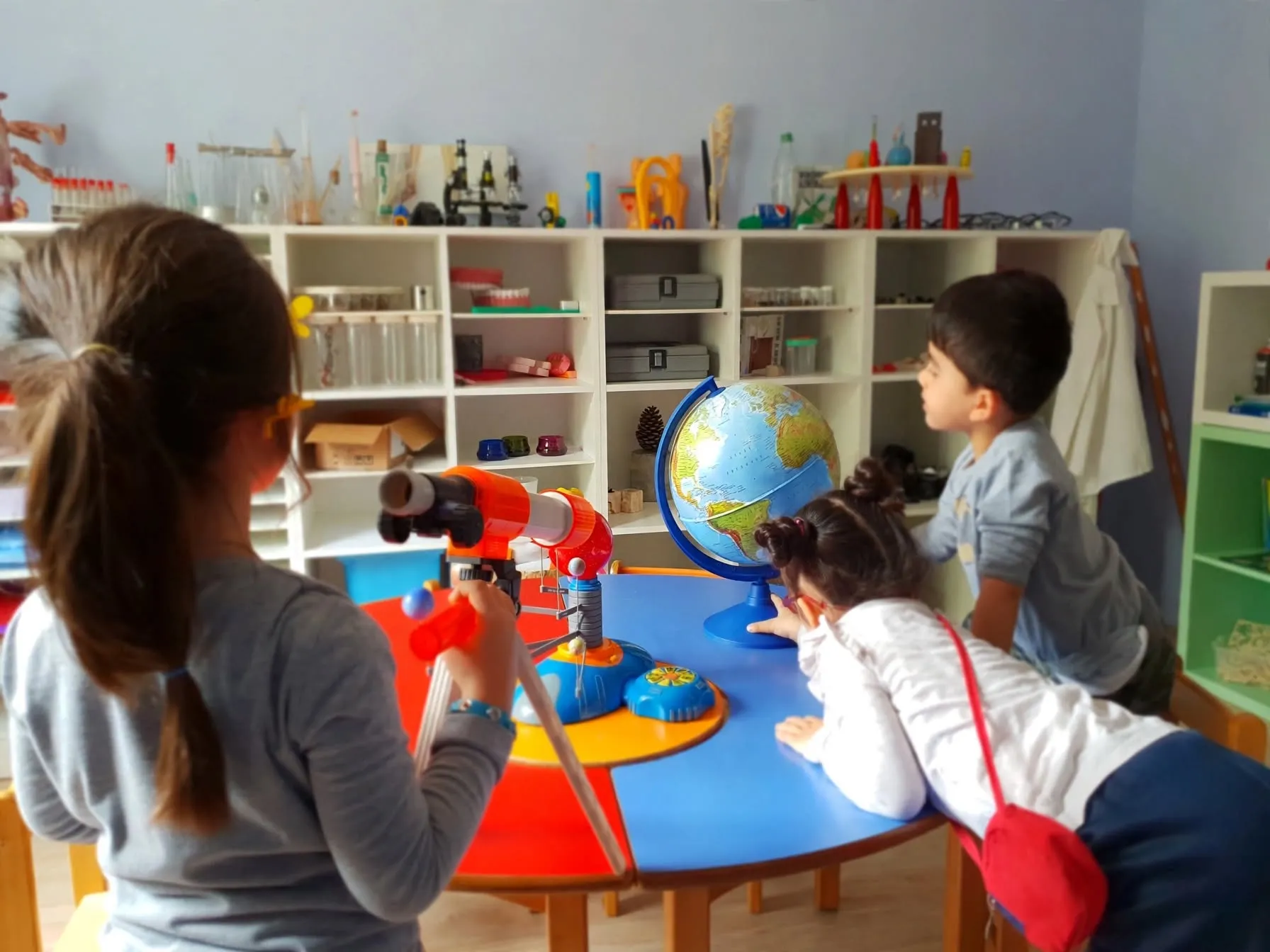 Bilim köşesinde teleskop ve dünya küresiyle inceleme yapan çocuklar